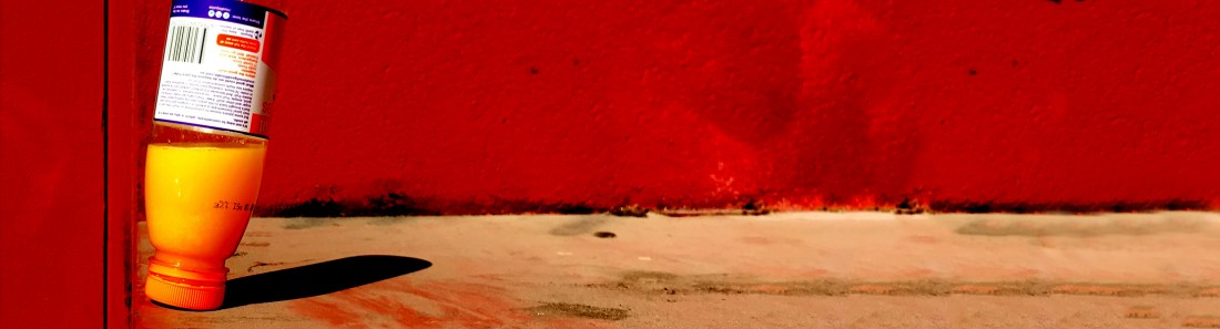 Upsidedown orange juice bottle on in street - slightly abstract